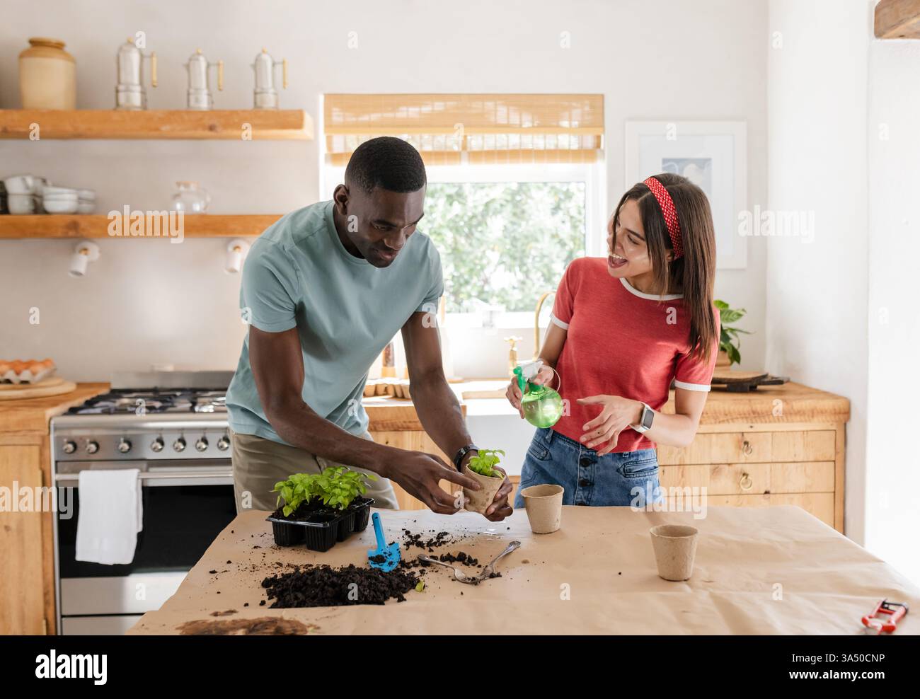 Diverse coppie che piantano erbe in cucina, godendosi il giardinaggio insieme a casa Foto Stock