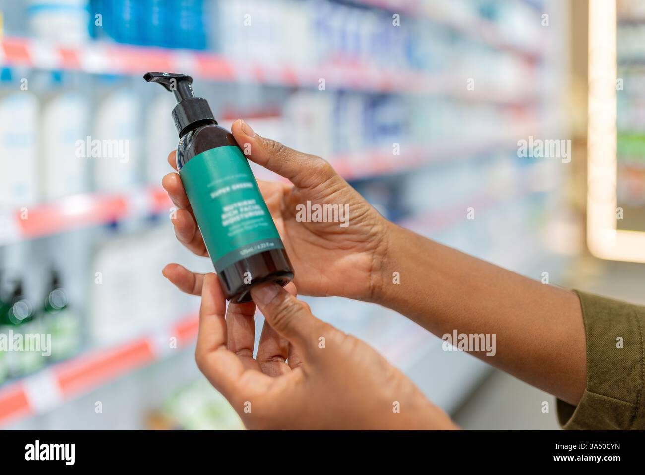 Primo piano di una mano tagliata che tiene una bottiglia e legge l'etichetta di un prodotto in una farmacia. Questo colpo ritagliato illustra i farmaci soggetti a prescrizione medica, la salute dei consumatori e le scelte al dettaglio. Foto Stock