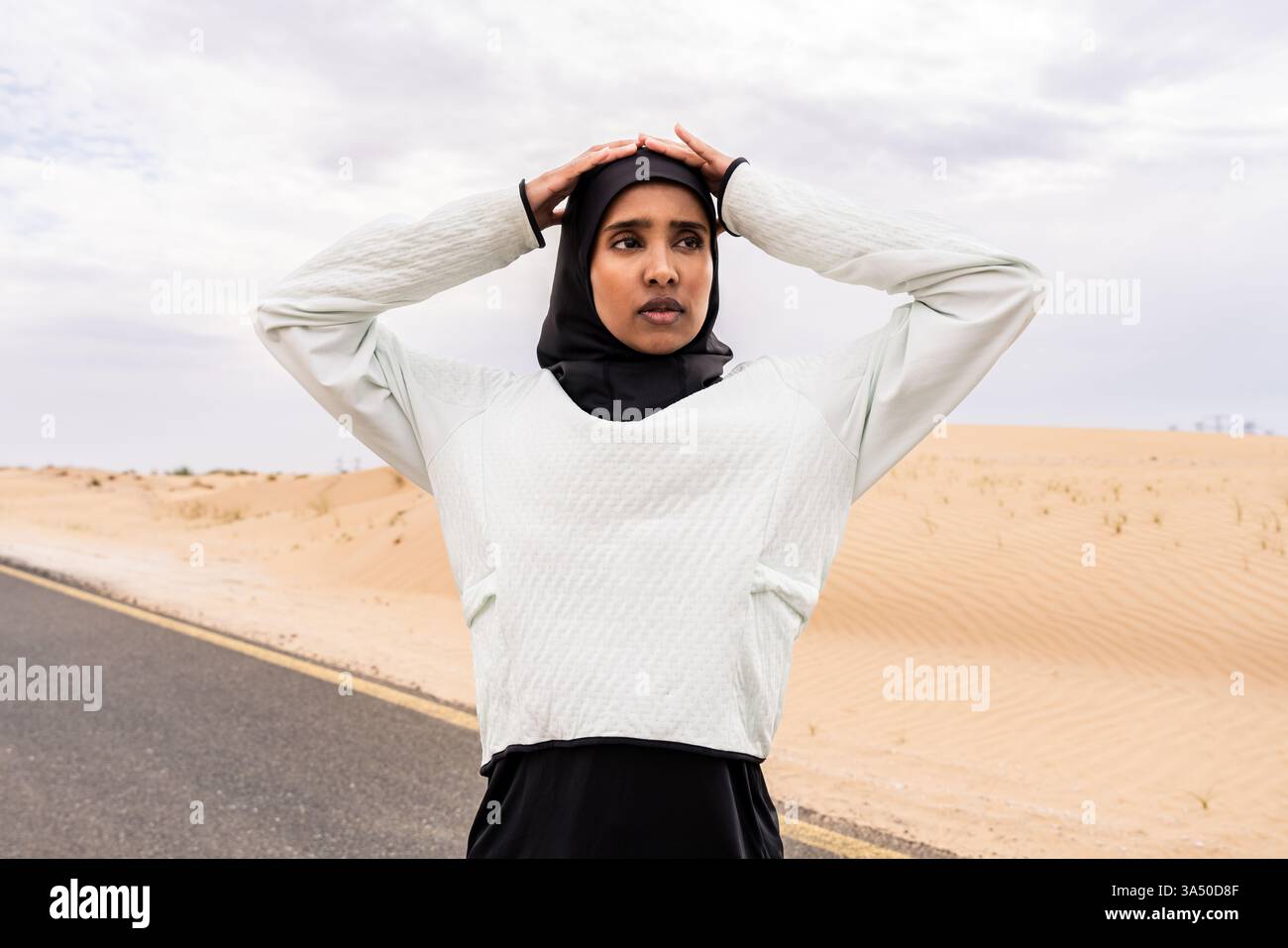 Una donna araba in un hijab si allena all'aperto in un ambiente desertico, una musulmana atletica in abbigliamento sportivo. La scena mette in evidenza il fitness all'aperto e uno stile di vita attivo in un paesaggio sabbioso. Foto Stock