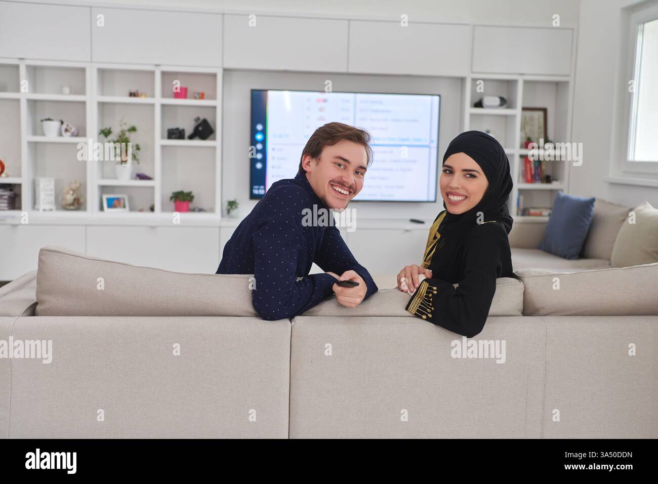 Giovane coppia musulmana che si diverte a casa durante il Ramadan, guardando la televisione insieme. Perfetto per la vita familiare, il Ramadan e le immagini della cultura islamica. Adatto per lo stile di vita e l'arredamento della casa o campagne multimediali. Foto Stock