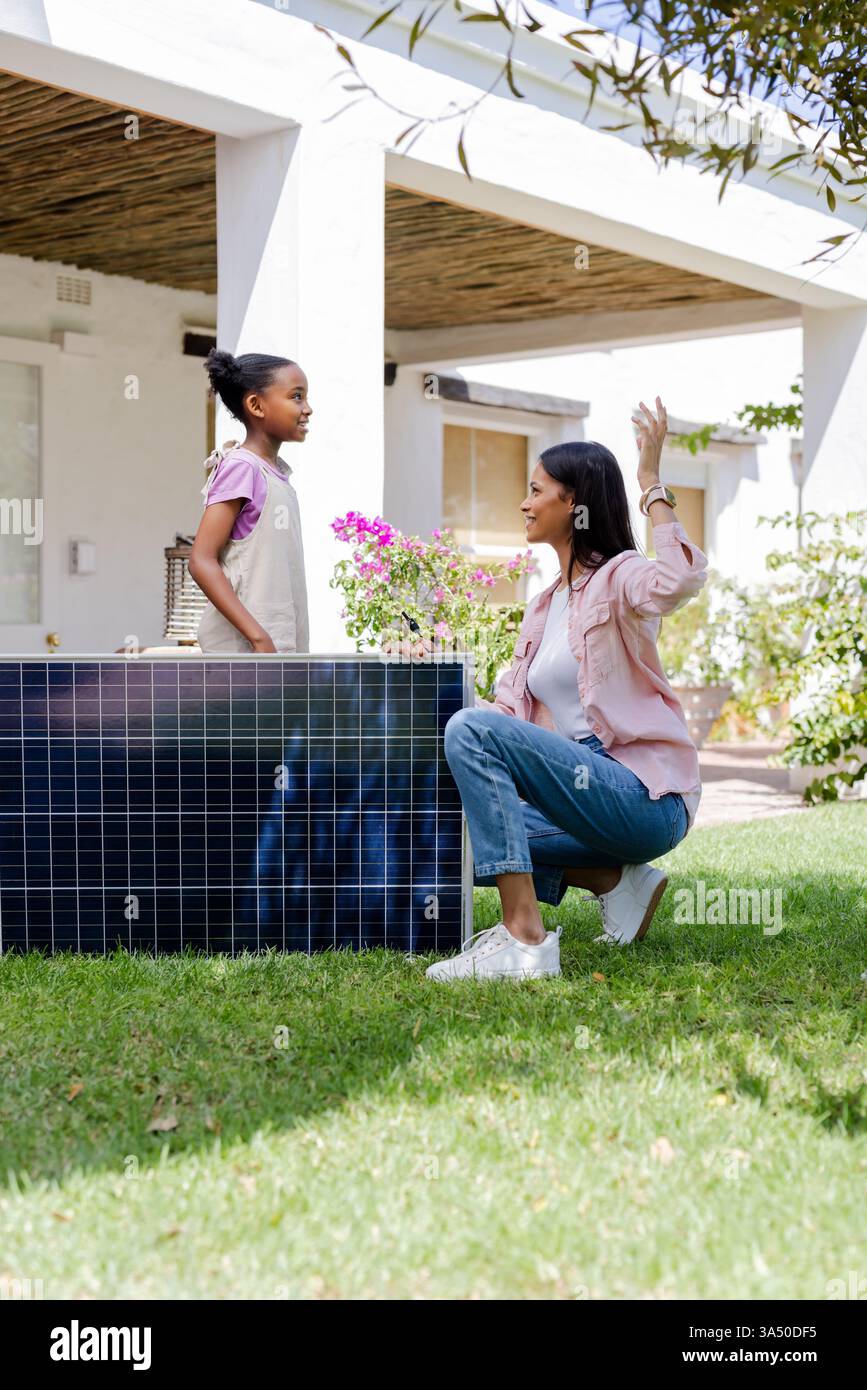 Madre e figlia discutono dell'installazione di pannelli solari nel soleggiato giardino sul retro, dello spazio di copia Foto Stock