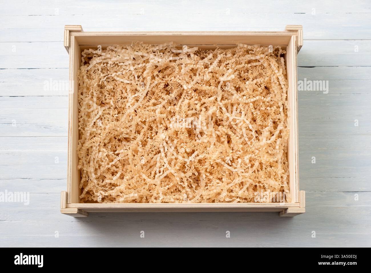 Scatola regalo vuota in legno con stucco di carta grattugiato naturale con taglio increspato su sfondo in legno blu chiaro Foto Stock