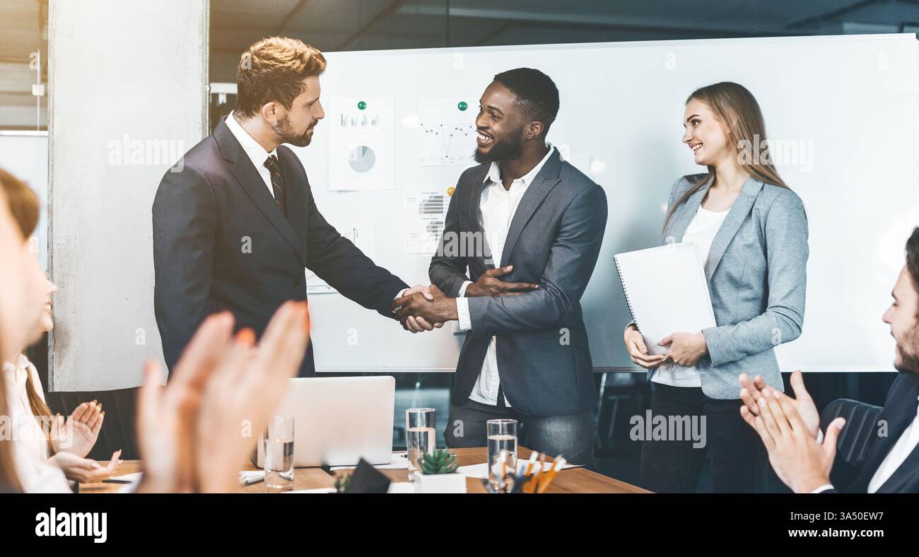 I professionisti di diverse origini stringono la mano dopo una riunione in una sala riunioni. Trasmette accordi, partnership e negoziati di successo. Ideale per comunicazioni aziendali e campagne di lavoro di squadra. Foto Stock