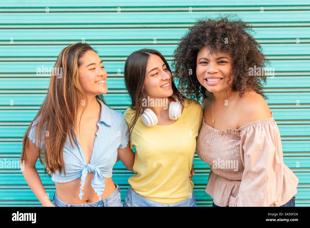Un gruppo eterogeneo di fidanzate sorridenti e sorridenti davanti alla telecamera contro un muro verde a Valencia, in Spagna. Un'immagine vivace e multirazziale, ideale per l'amicizia, i viaggi e i temi delle donne. Foto Stock