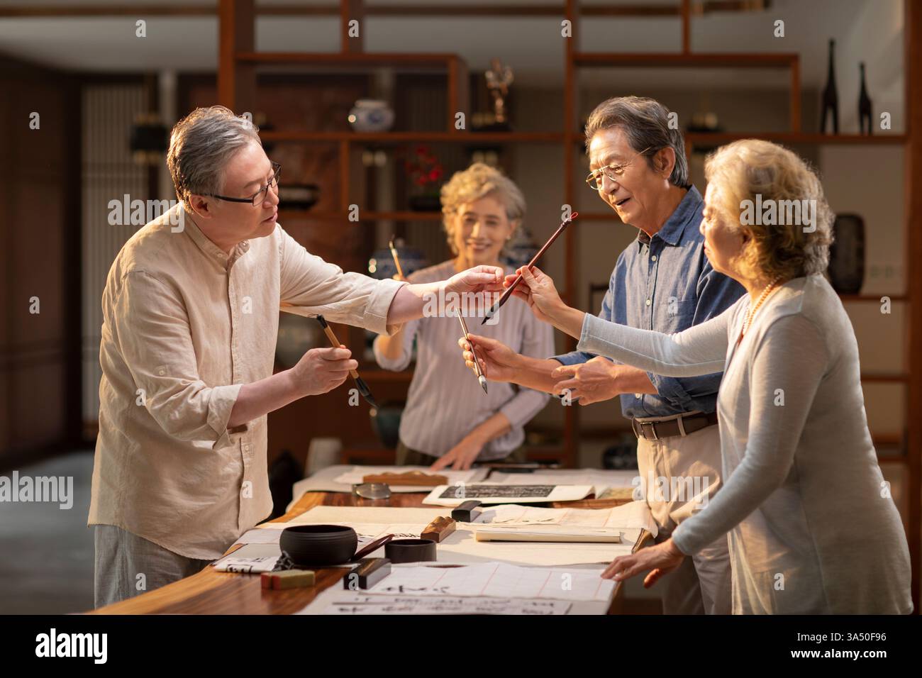 Gruppo di uomini e donne cinesi anziani che praticano calligrafia a casa, in piedi intorno a un tavolo. Questa attività culturale mette in evidenza il patrimonio culturale, l'apprendimento e lo stile di vita degli anziani in un ambiente domestico. Adatto per l'educazione, le arti e le tradizioni e per il benessere degli adulti più anziani. Foto Stock