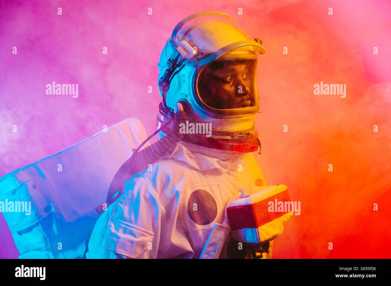 Ritratto cinematografico di un uomo in una tuta spaziale, che offre un'atmosfera vivace di esplorazione spaziale. L'illuminazione colorata conferisce all'immagine un'audace sensazione fantascientifica. Adatto per il branding di tecnologia, scienza e avventura. Foto Stock