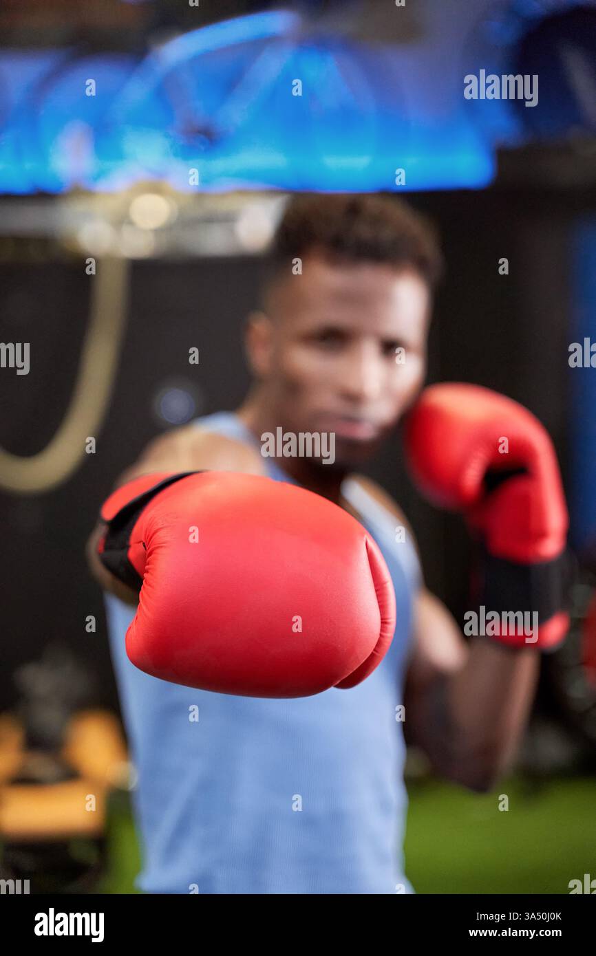 Primo piano sul pugno con i guanti di un pugile nero forte, pronto per un pugno potente sul ring. Questa foto sportiva mirata enfatizza la forza, l'allenamento e la competizione nel pugilato. Foto Stock