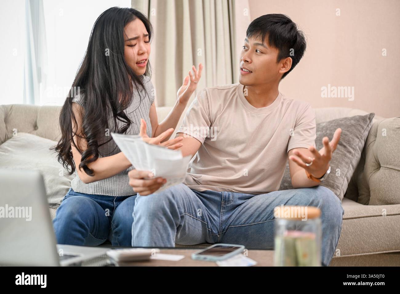 Una moglie asiatica risentita e arrabbiata sta discutendo sulle fatture delle famiglie e sulle alte bollette domestiche, litigando sulla questione dello spreco di m Foto Stock