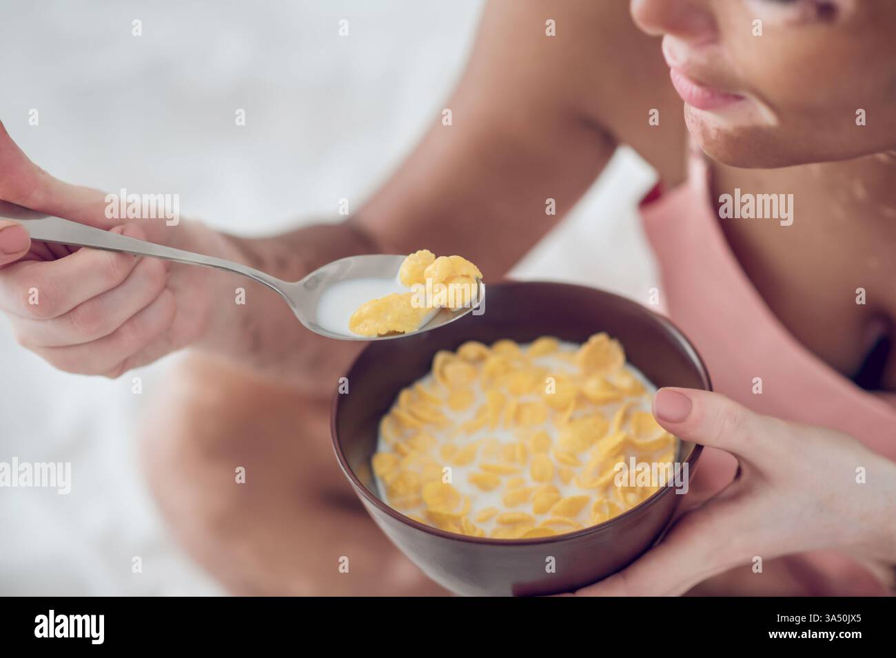 Donna mista con vitiligine che mangia cereali mentre si rilassa sul letto di casa. Ottimo per immagini di stile di vita inclusivo, benessere e scene per la colazione di tutti i giorni. Foto Stock