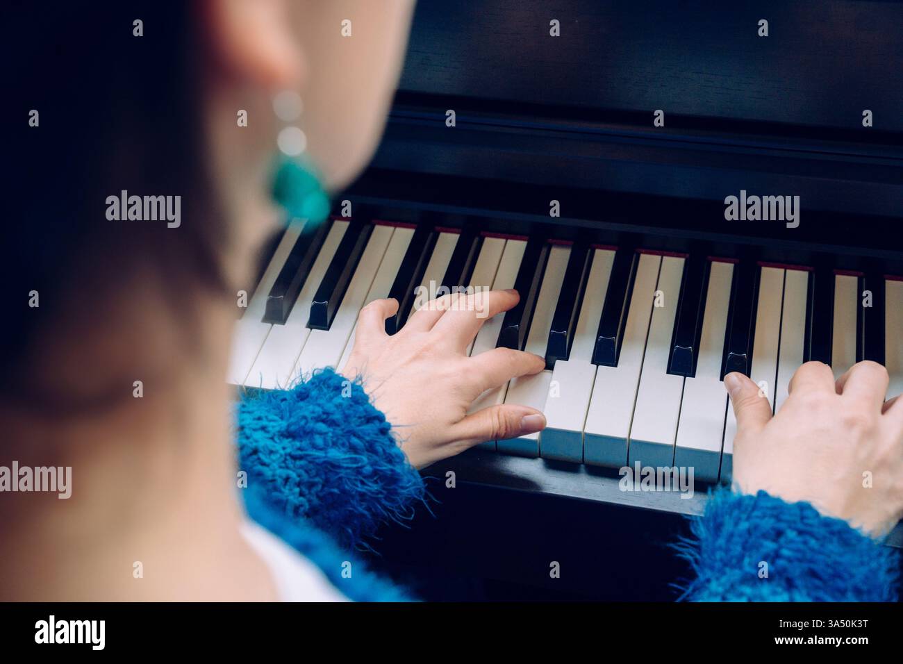 Primo piano delle mani su una tastiera del piano, mentre una donna irriconoscibile pratica a casa. La scena suggerisce l'insegnamento, l'apprendimento e la dedizione musicale. Foto Stock