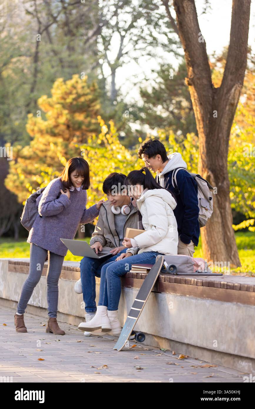 Gli studenti universitari cinesi felici utilizzano un notebook nel campus, che mostra la vita degli studenti e la loro collaborazione. Ideale per l'istruzione, la tecnologia e la grafica del lavoro di squadra del campus con un'atmosfera allegra. Foto Stock