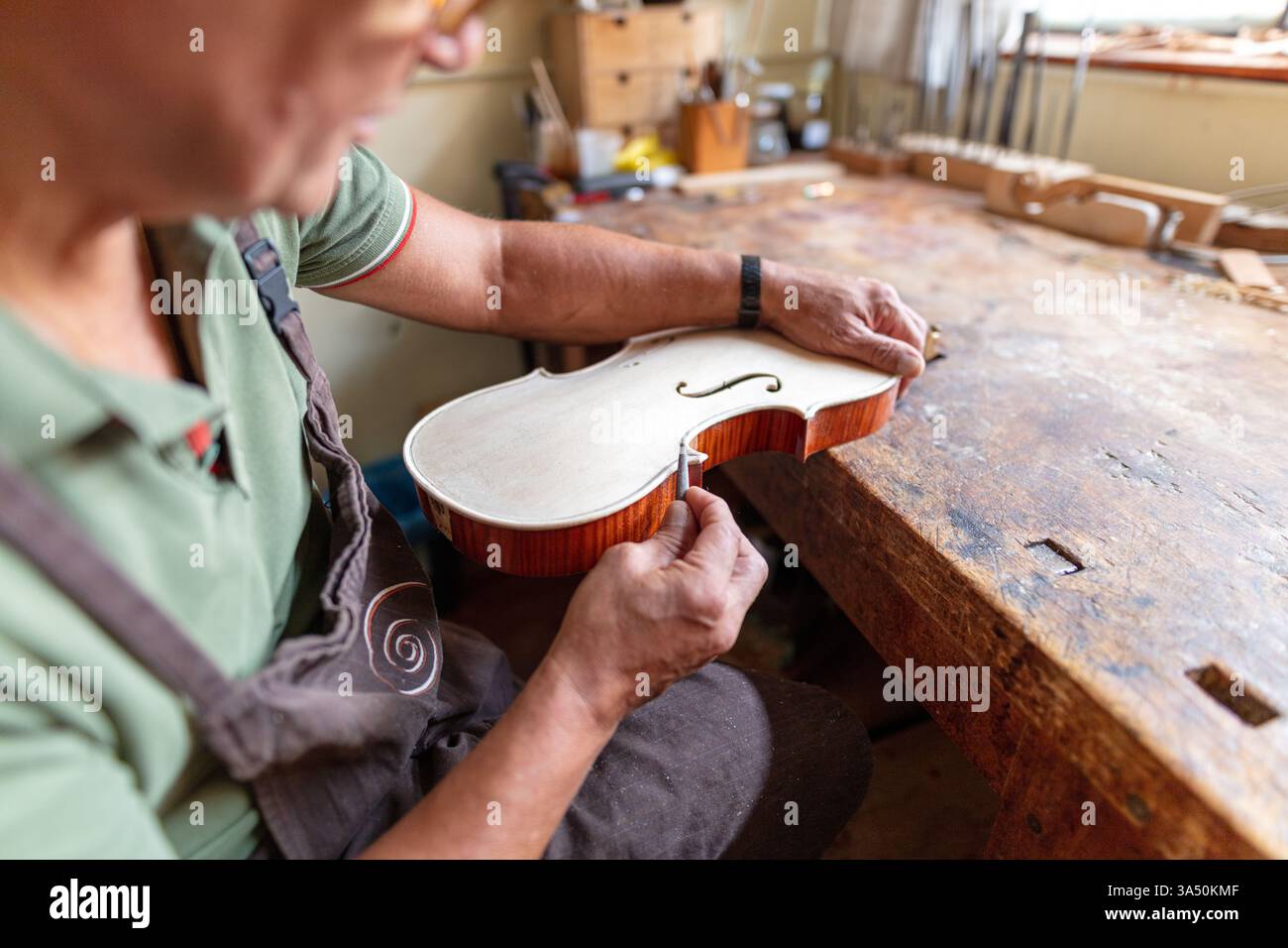 Liutaio al lavoro in un tradizionale laboratorio italiano. Un abile artigiano circondato da strumenti e strumenti, che mette in risalto l'artigianato, l'esperienza liutai e il patrimonio musicale italiano. Foto Stock