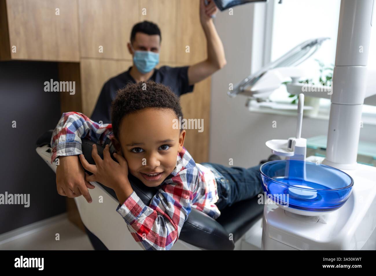 Bambino dalla pelle scura sdraiato su una sedia dentale in una clinica. Temi di salute infantile e odontoiatria pediatrica con un'atmosfera amichevole e accessibile. Ambiente per studi dentistici interni adatto per comunicazioni sanitarie. Foto Stock