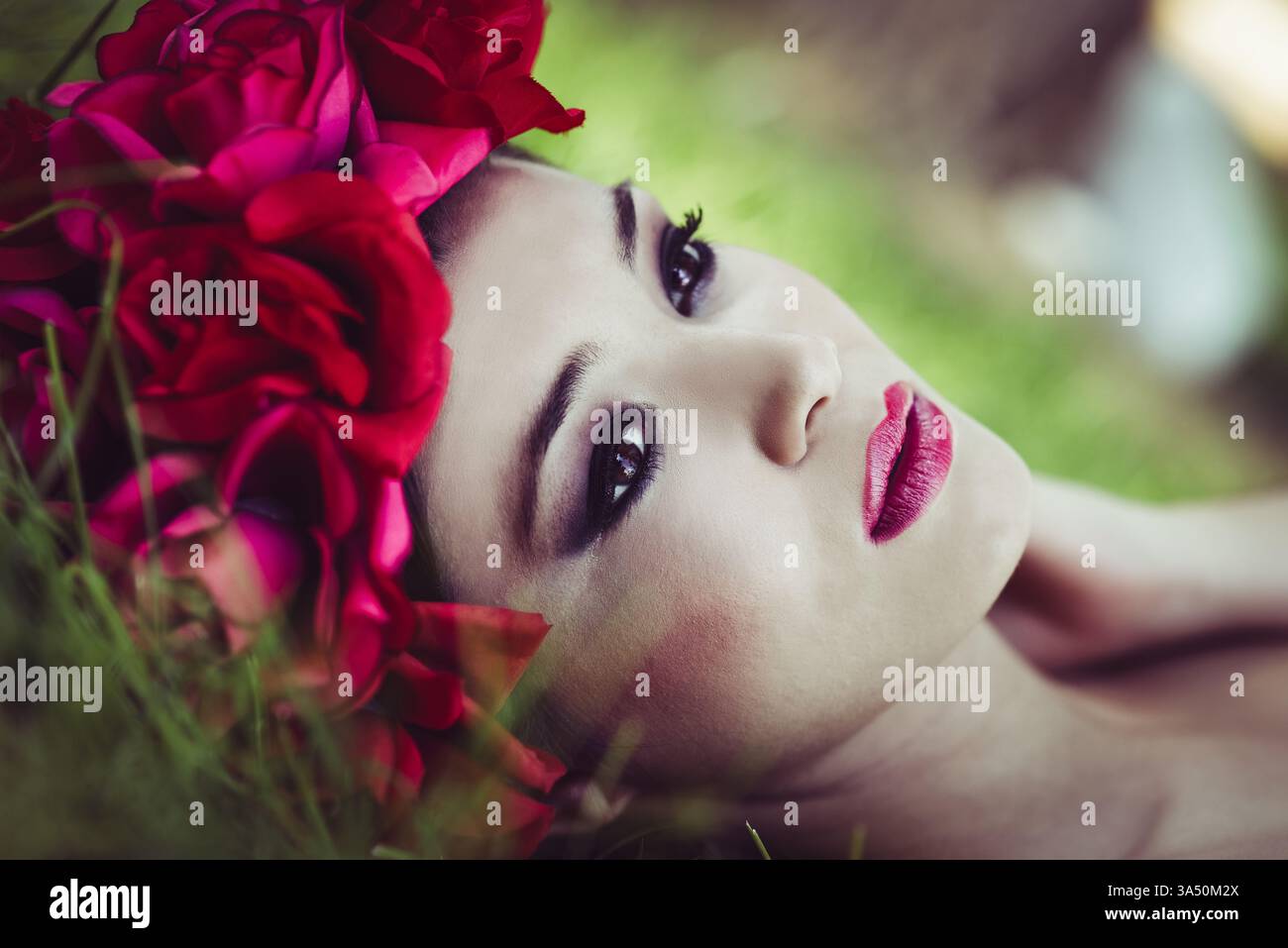 Donna asiatica con ghirlande di fiori sulla testa che guarda lontano sdraiata sull'erba nel parco durante il giorno Foto Stock