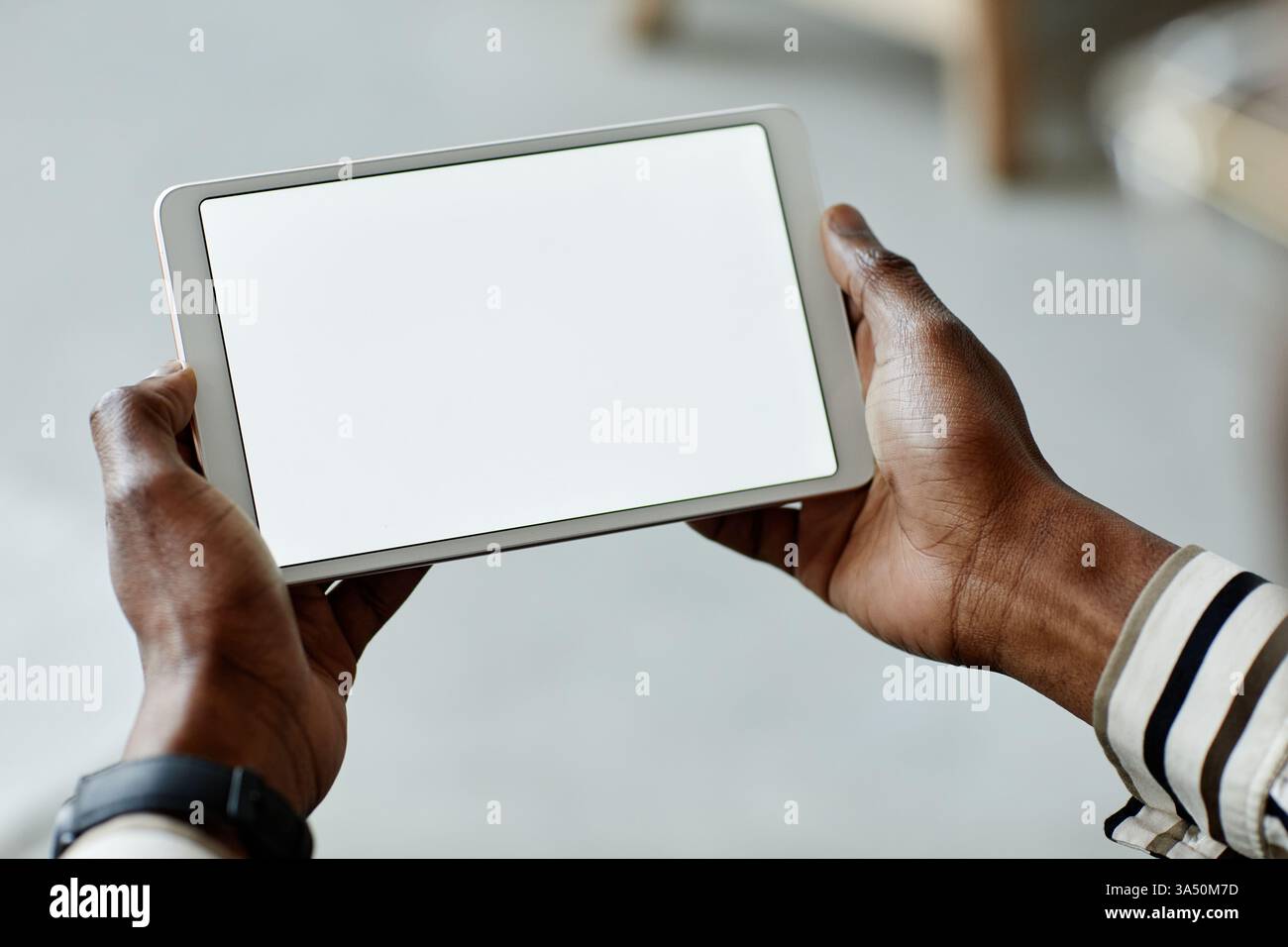 Primo piano di un afroamericano che tiene in mano un tablet con uno schermo vuoto mentre utilizza dispositivi domestici intelligenti. La scena trasmette l'automazione domestica e la tecnologia wireless in un ambiente interno moderno, con spazio di copia per la messaggistica. Foto Stock