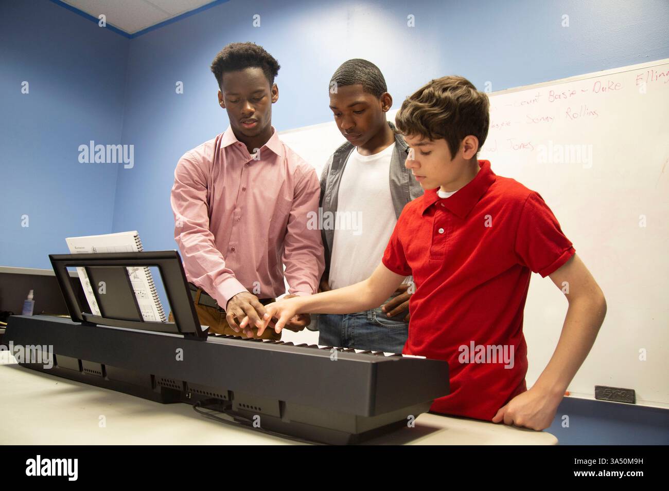 Il mentore afroamericano insegna il piano ai giovani adolescenti in classe. La scena mette in risalto il tutoraggio e l'educazione musicale, con gli studenti al pianoforte e un istruttore di guida. Ideale per programmi post-scuola, formazione musicale e sviluppo giovanile. Foto Stock