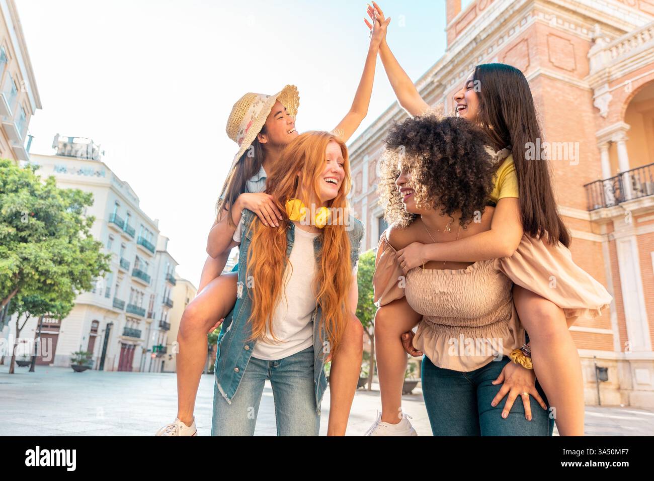 Da un punto di vista basso, un allegro gruppo di donne diverse siedono insieme in una strada di Valencia, tenendosi per mano e sorridendo. La scena cattura l'amicizia e la vivace vita urbana in Spagna. Foto Stock