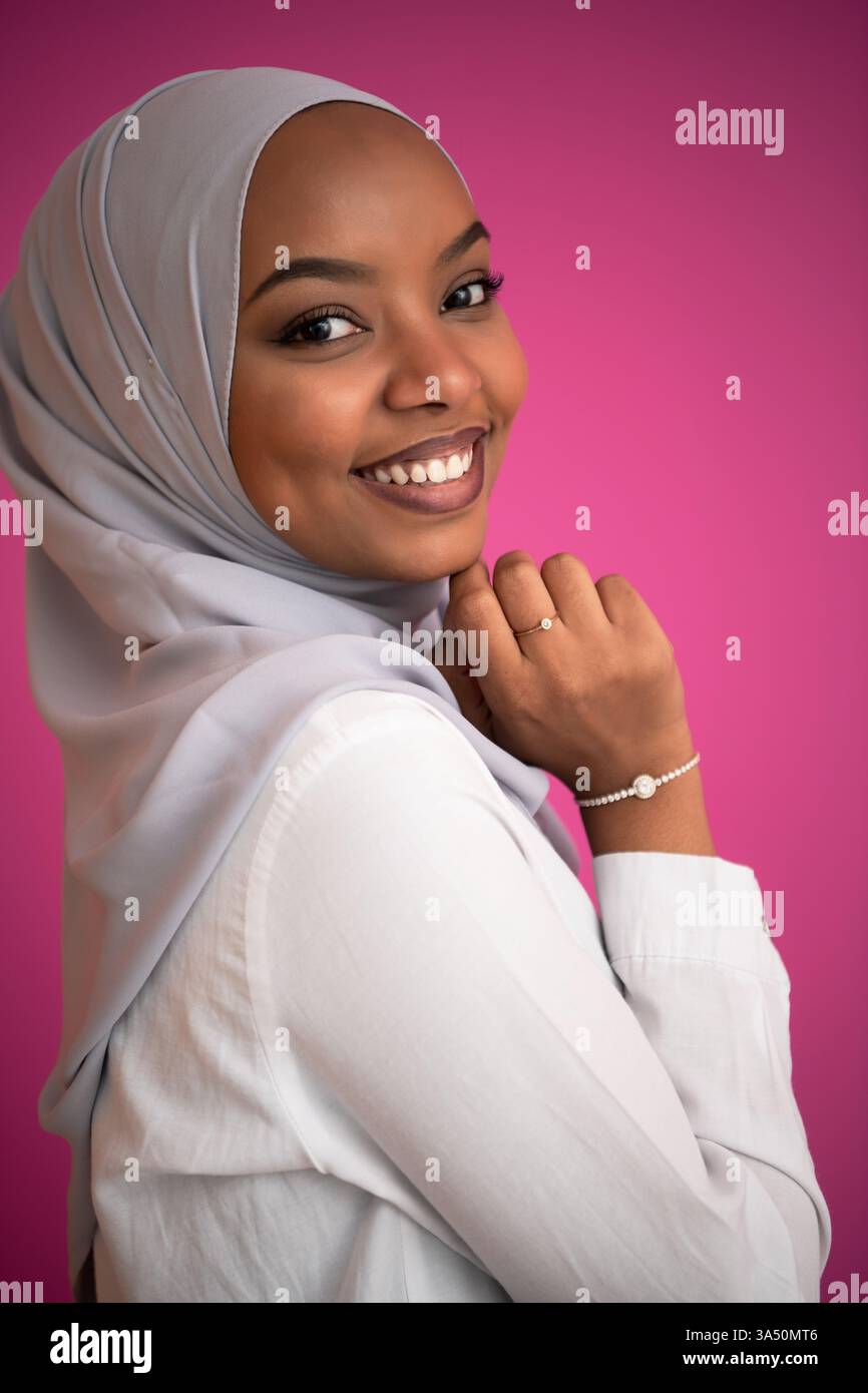Giovane donna afro che indossa un tradizionale abbigliamento islamico su uno sfondo rosa brillante. Questo audace ritratto in studio mette in risalto la moda hijab, la cultura e la bellezza moderna. Foto Stock