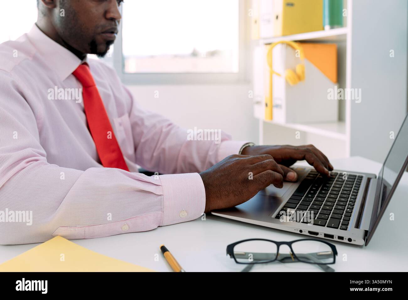 Vista laterale di un imprenditore nero che lavora su un netbook in un ufficio moderno. Ideale per le aziende, l'imprenditorialità e le immagini dei concept sul luogo di lavoro. Foto Stock