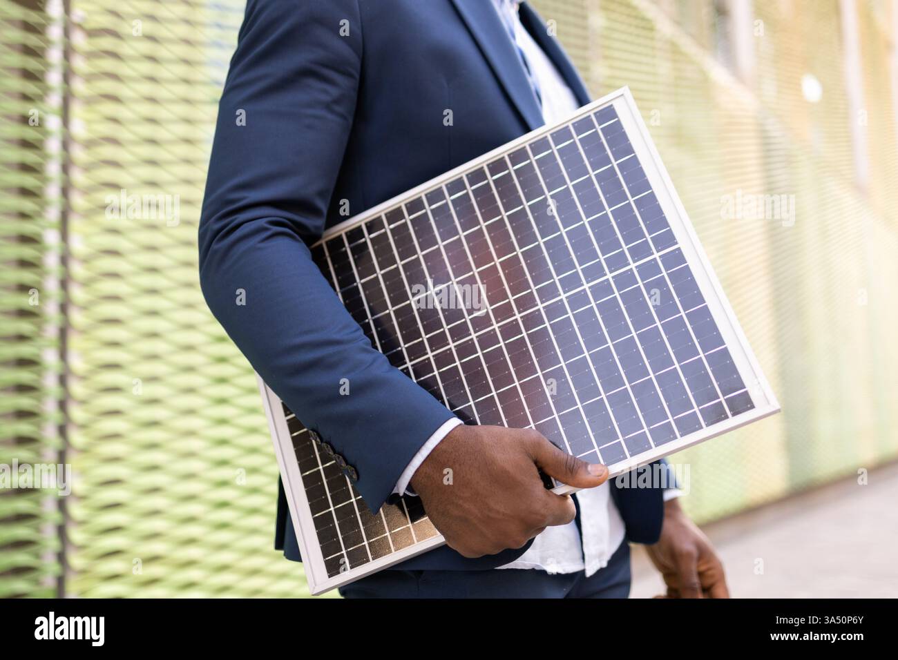 Vista ritagliata di un uomo d'affari nero senza volto che detiene un pannello solare, simboleggia l'energia rinnovabile e l'innovazione sostenibile. L'abbigliamento formale all'aperto e un moderno concetto energetico rendono questa immagine adatta per le campagne di sostenibilità aziendale e di tecnologia verde. Un'ottima soluzione per progetti incentrati sull'energia, l'ambiente e il futuro. Foto Stock