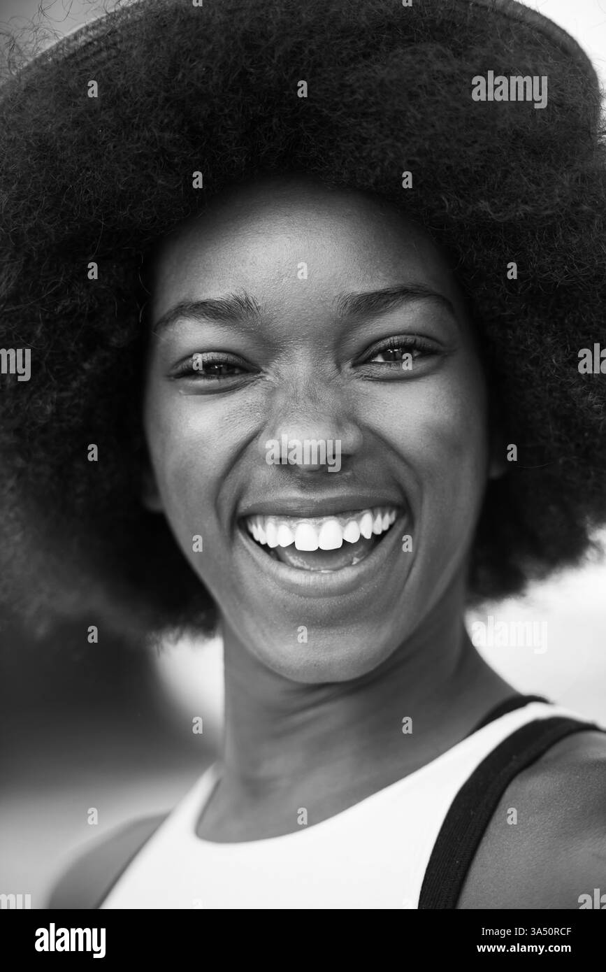 Ritratto ravvicinato di una giovane donna nera sorridente e che guarda in alto in una giornata di sole. La vivace foto all'aperto trasmette fiducia e felicità, adatta a campagne di bellezza, stile di vita e moda. La luce naturale del sole e l'espressione allegra esaltano l'atmosfera positiva. Foto Stock