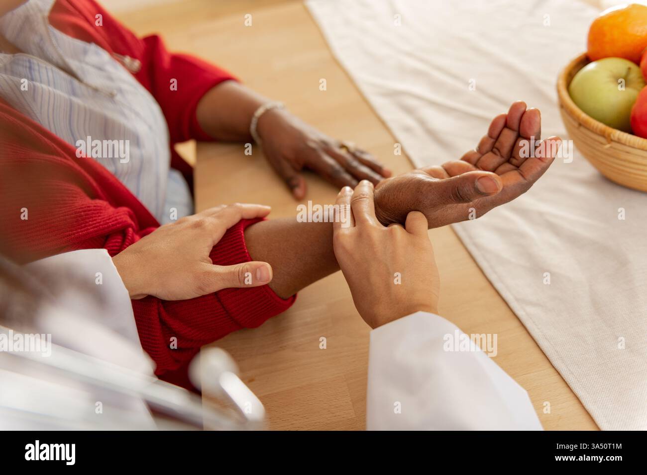 Una donna nera medico controlla il polso di una donna nera a casa, illustrando l'assistenza sanitaria domiciliare. L'ambiente domestico comunica il supporto medico accessibile e il benessere domestico. Ideale per l'assistenza sanitaria, i servizi infermieristici e il marketing per la cura dei pazienti. Foto Stock