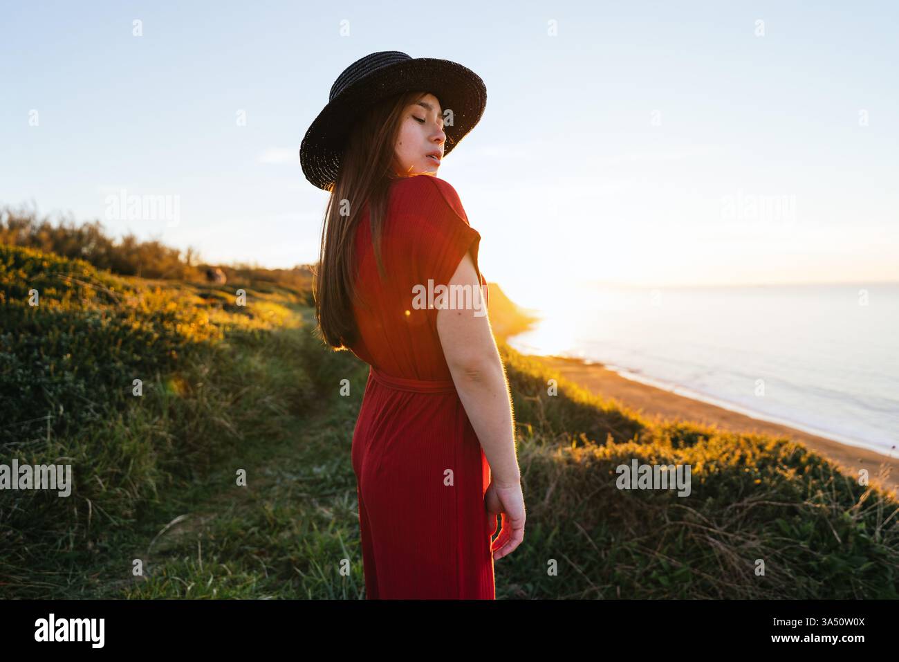 Donna asiatica in piedi su un campo erboso che guarda le spalle all'aperto durante il tramonto Foto Stock