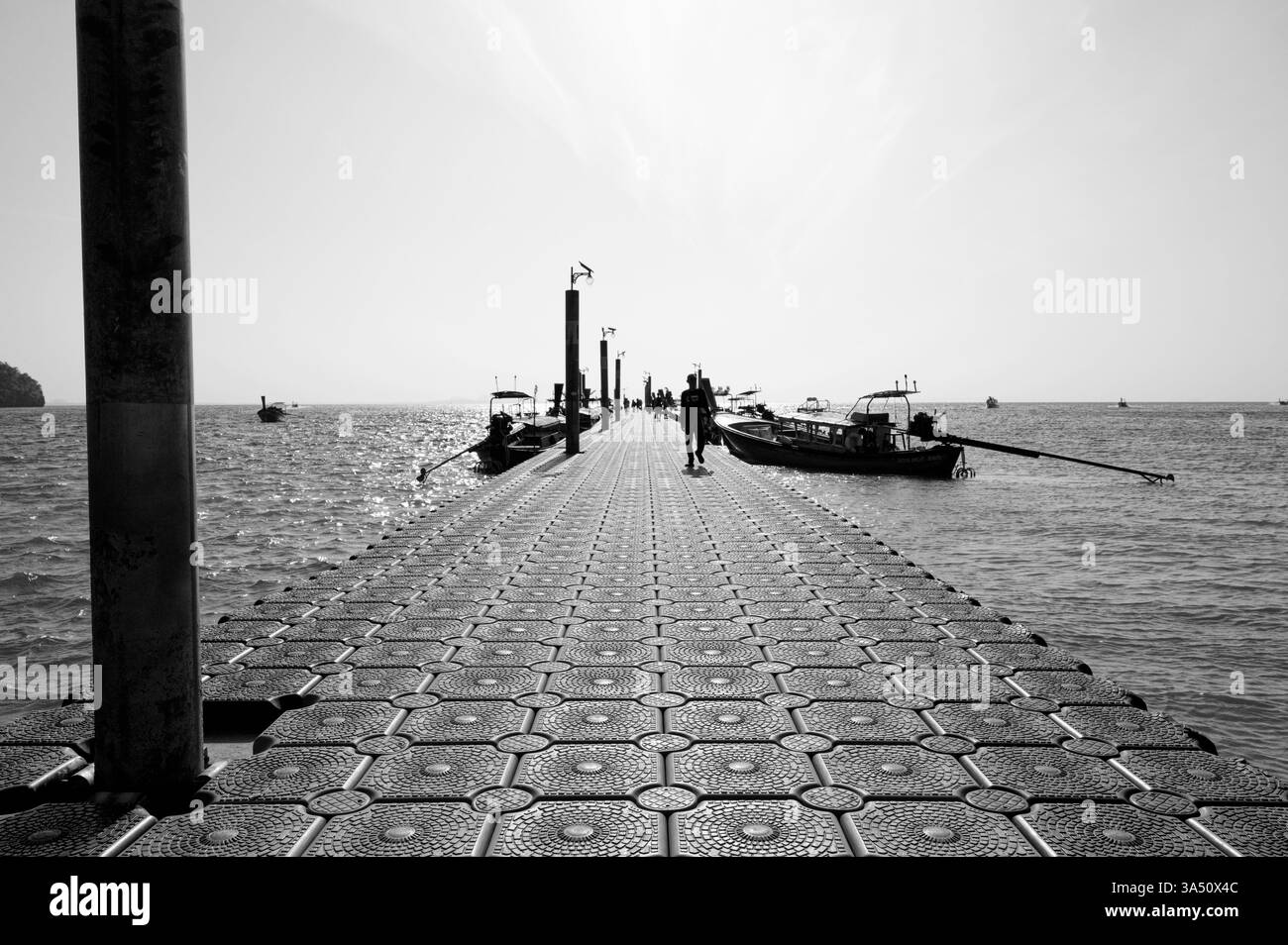 Un viaggiatore cammina lungo un molo galleggiante fiancheggiato da barche a coda lunga a Railay Foto Stock