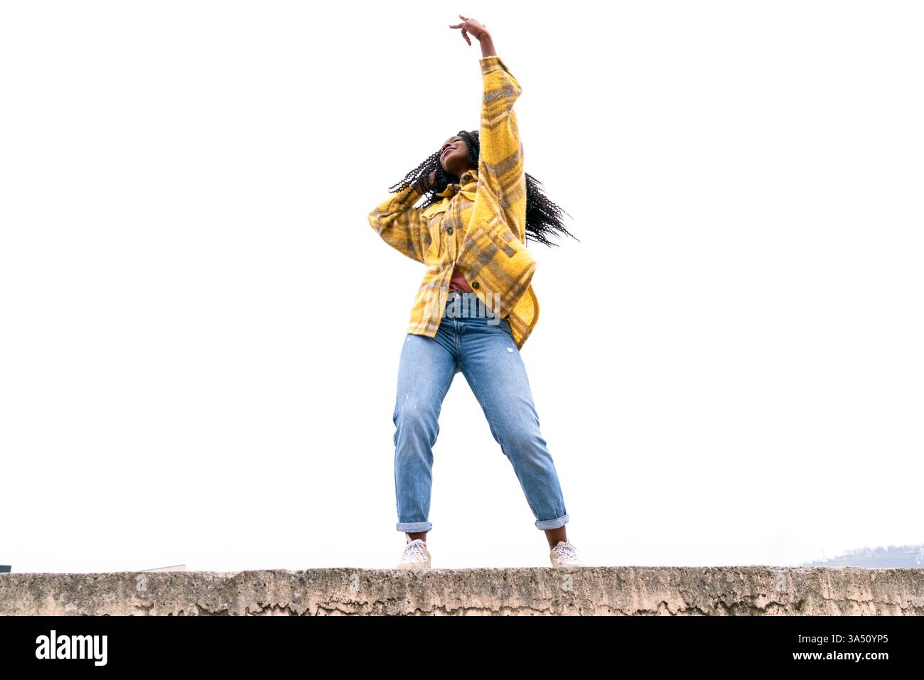 Donna nera che balla in un parco con le braccia tese in movimento espressivo. La scena all'aperto cattura energia spensierata e movimento dinamico. Ideale per campagne di lifestyle, benessere e messaggi positivi. Foto Stock