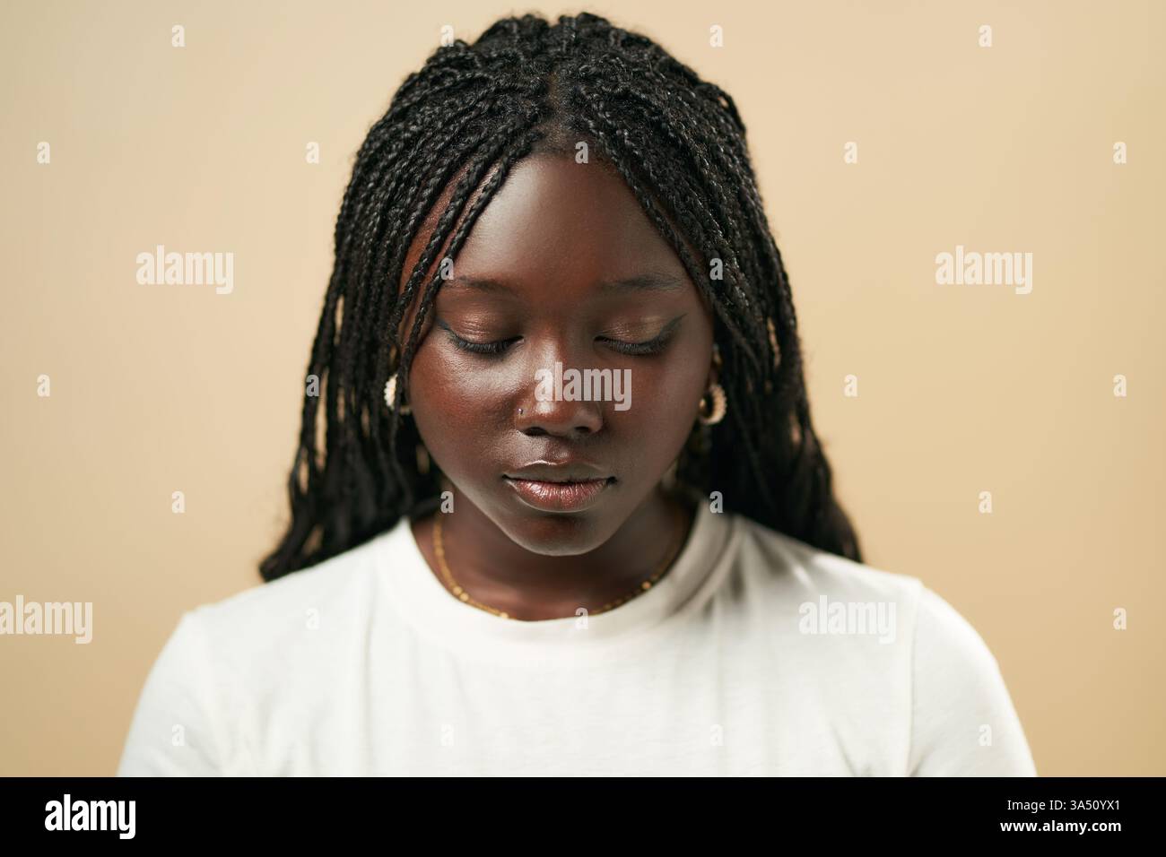Ritratto di una giovane donna afroamericana con trecce afro in un pullover bianco sullo sfondo di uno studio beige. Ideale per la moda, i ritratti e la fotografia in studio. Foto Stock