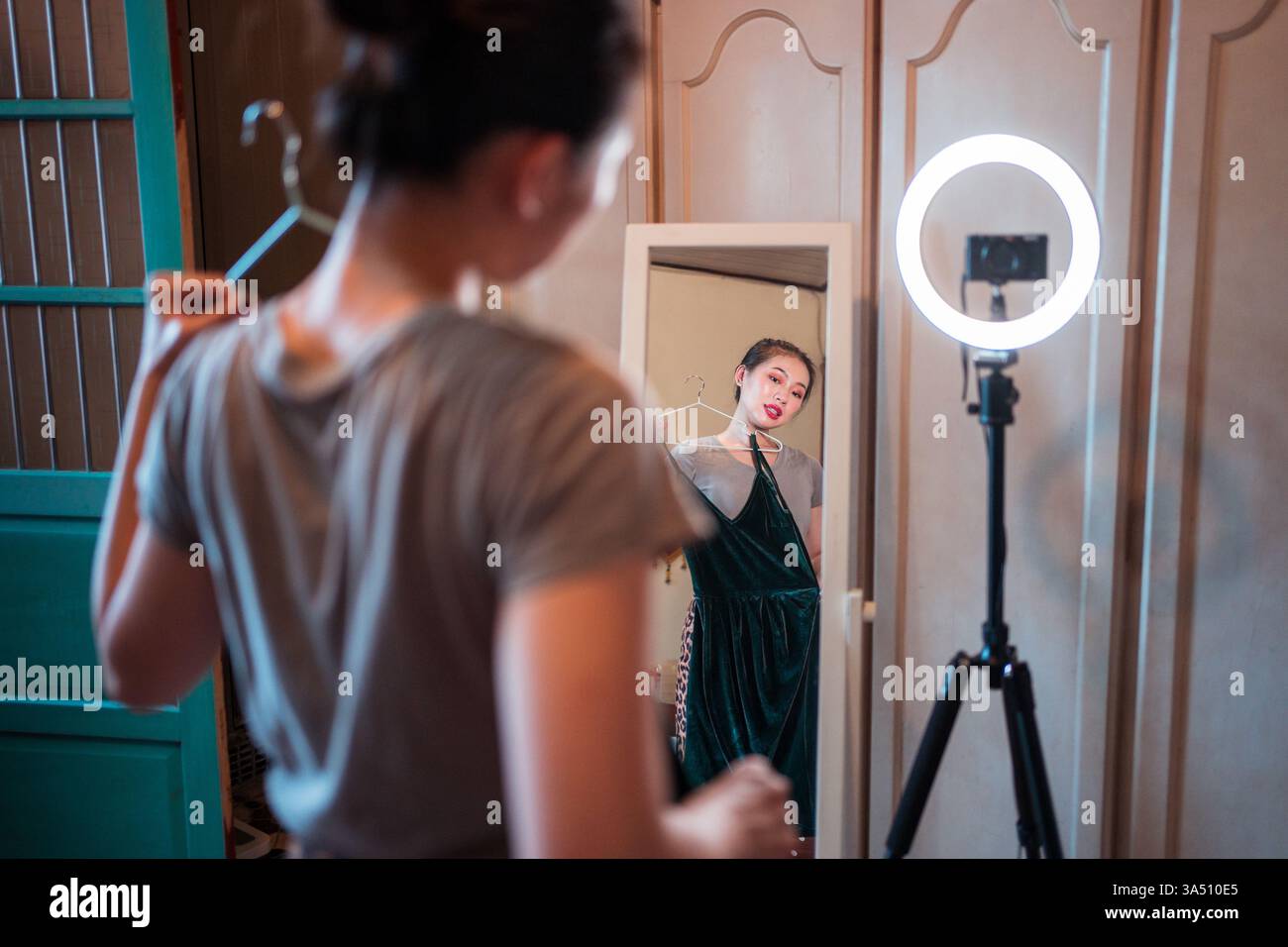 La donna asiatica registra un video di abbigliamento di moda davanti a uno specchio. Questa configurazione per home studio con illuminazione e attrezzatura per fotocamera funziona bene per la moda, la bellezza e i contenuti influencer sui social media. Ideale per campagne di e-commerce e lifestyle. Foto Stock