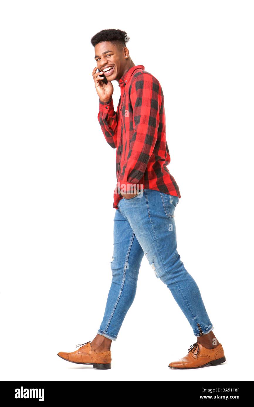 Uomo nero sorridente mano in tasca mentre parla al telefono mentre cammina su sfondo bianco Foto Stock