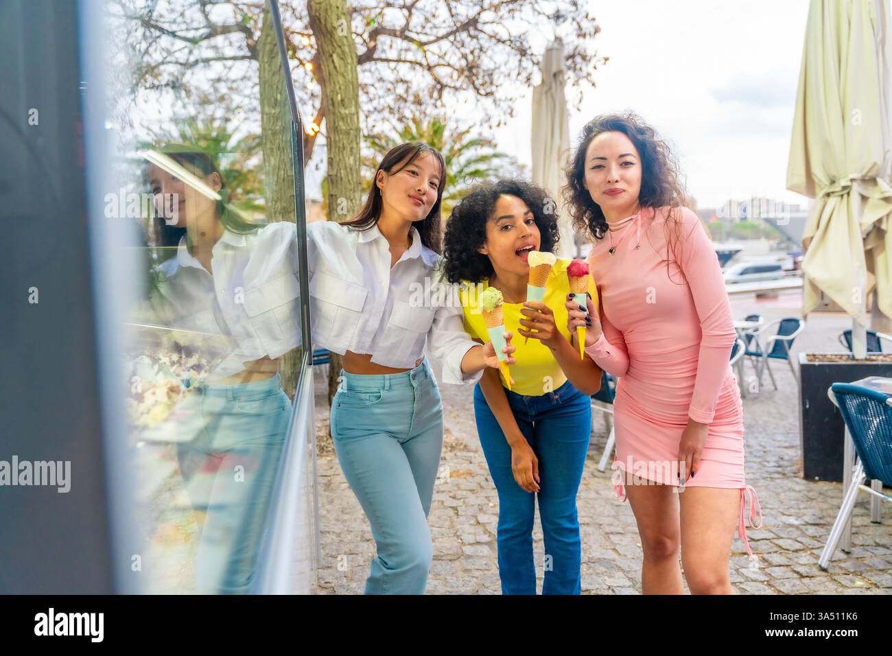 Tre donne di bellezza multietnica che mangiano gelati accanto al negozio in strada Foto Stock