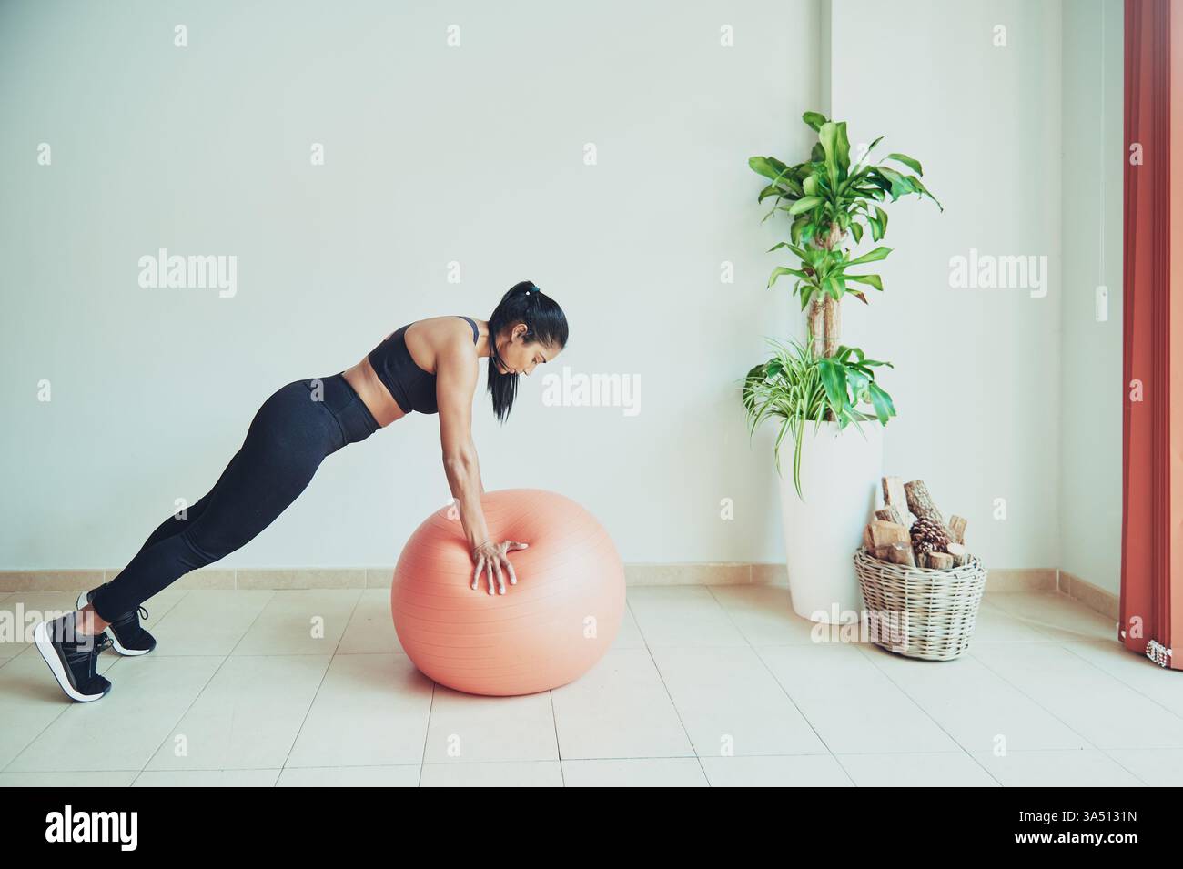 Donna ispanica che si piega in avanti su una palla fitness durante l'allenamento a casa Foto Stock