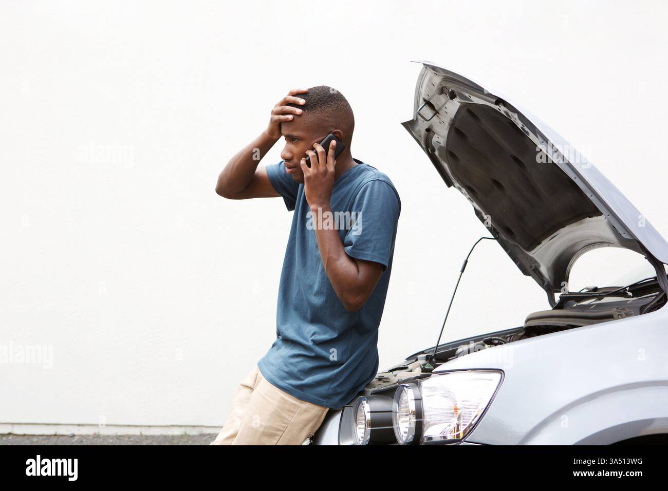 Ritratto di un uomo stressato al telefono che richiede assistenza stradale per un guasto alla vettura. Un ambiente all'aperto che trasmette problemi automobilistici e servizi urgenti, ideale per l'assistenza stradale o i contesti assicurativi. Utile per materiali di marketing sui servizi di assistenza auto, supporto di emergenza e comunicazione con i clienti. Foto Stock
