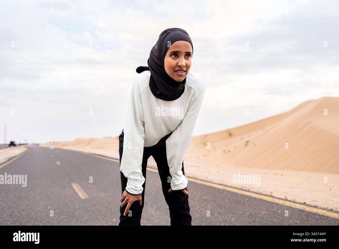 Bella donna araba del Medio Oriente che indossa l'hijab all'aperto in un ambiente desertico. Questa dinamica immagine sportiva all'aperto si adatta alle campagne di fitness, running o lifestyle atletico con un tocco di modernità. Foto Stock