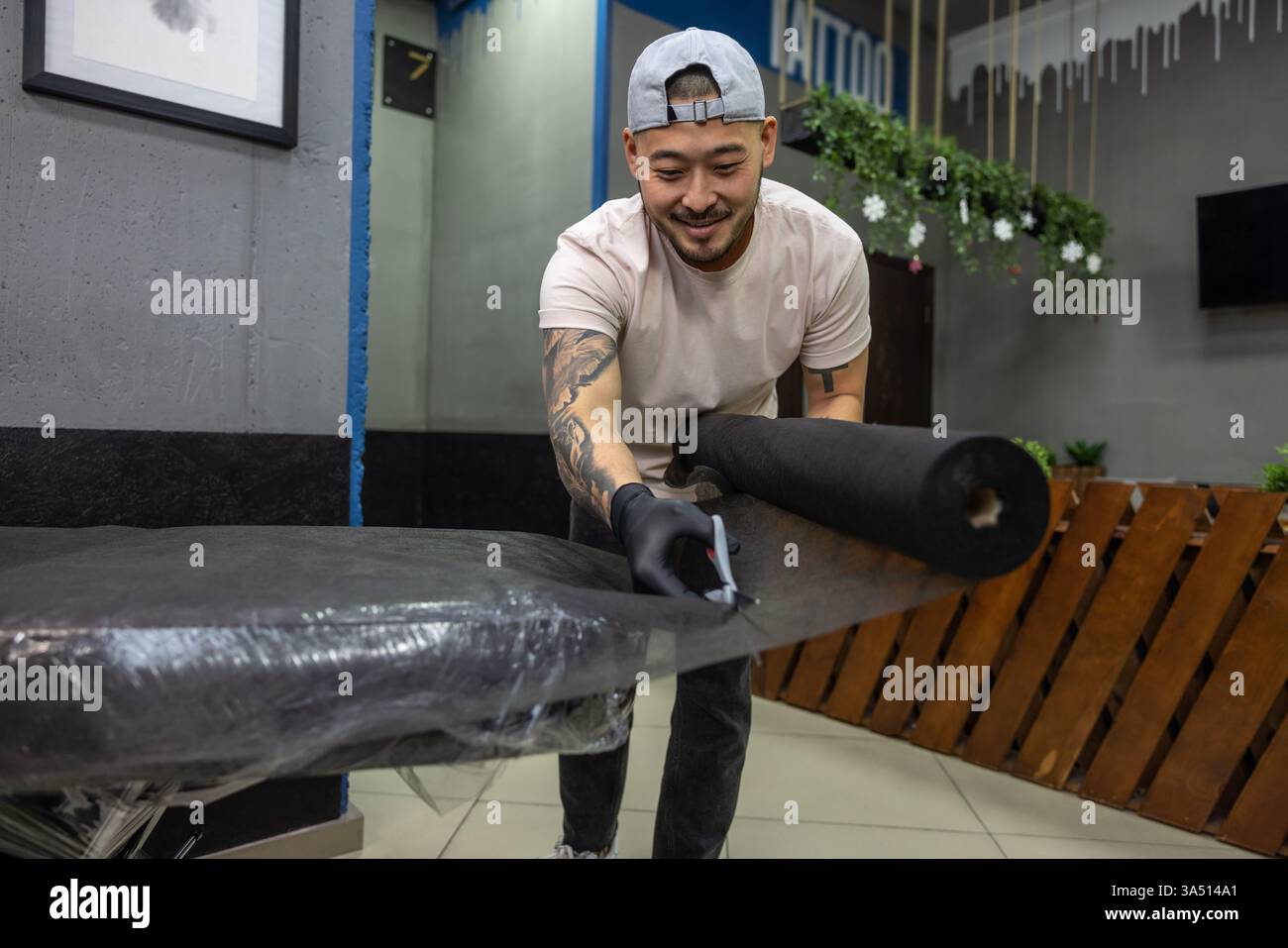 Il maestro asiatico del tatuaggio prepara il divano in uno studio di tatuaggio, pronto per una sessione. Un ambiente di body art professionale adatto a studi, inchiostri e temi di design. Foto Stock