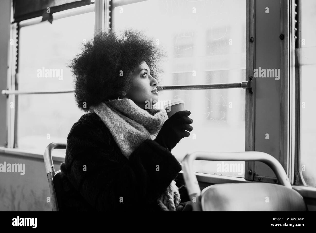 Bella donna con un ritratto Afro tagliato di capelli sui mezzi pubblici in un ambiente urbano. La candida immagine in stile Street si adatta ai temi di viaggi, spostamenti e stile di vita cittadino con un'atmosfera contemporanea. Foto Stock