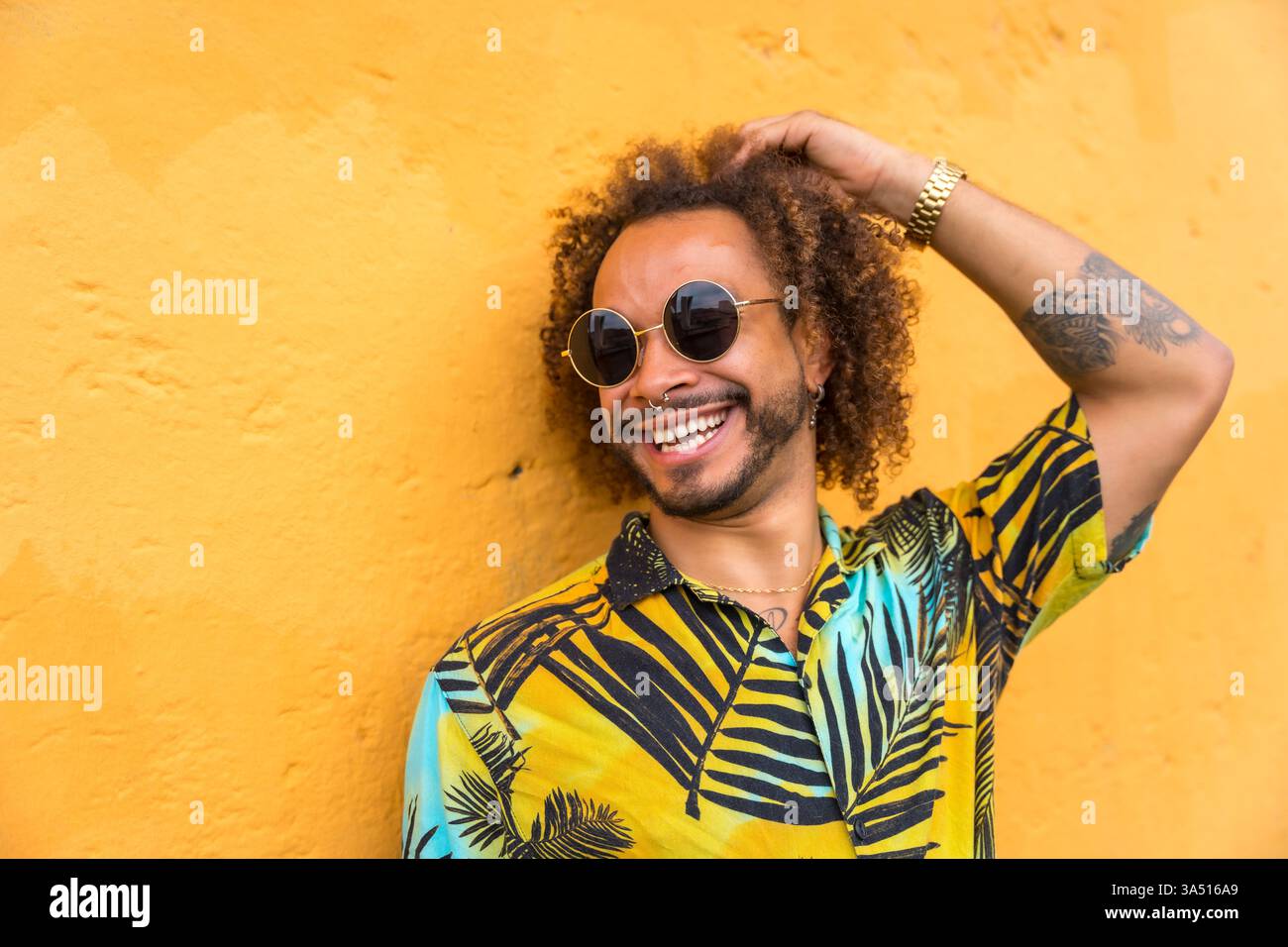 Uomo con acconciatura afro che indossa una camicia con stampa palma su sfondo giallo brillante. L'immagine di questo lifestyle estivo trasmette calore e positività, adatta per la moda, l'abbigliamento casual e le campagne a tema tropicale. Perfetto per titoli e testi promozionali con colori in grassetto. Foto Stock