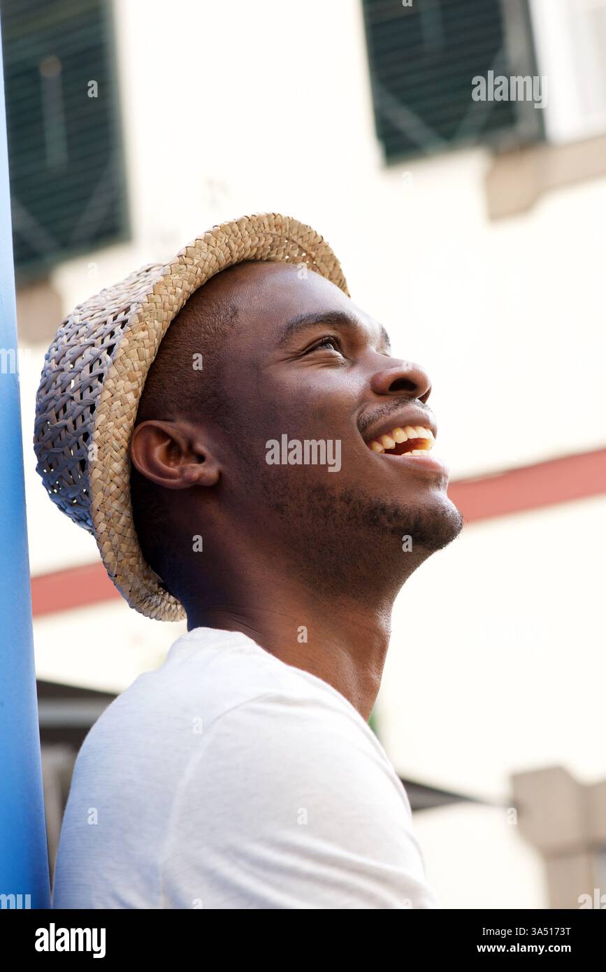 Ritratto laterale di un uomo afroamericano felice che indossa un cappello, che guarda in alto. L'ambiente esterno e la posa casual ed elegante conferiscono a questa immagine un ampio fascino per progetti di stile e moda. Ideale per campagne ottimistiche sulla fiducia e sui momenti ottimistici. Foto Stock