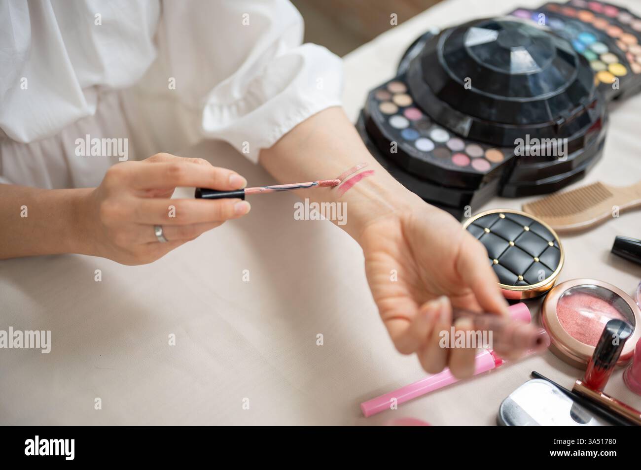 Primo piano di una beauty blogger che guarda i rossetti sul braccio, mostrando cosmetici colorati. La scena include una scrivania da trucco e prodotti per il trucco, che trasmettono la creazione di contenuti di bellezza. Ideale per cosmetici e influencer marketing. Foto Stock