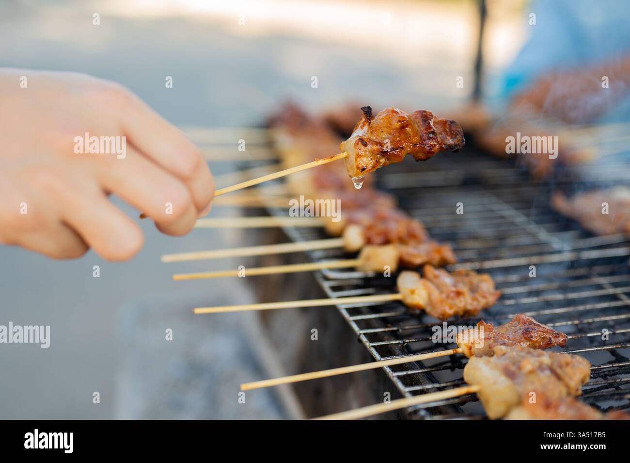 Primo piano di un delizioso spiedino di maiale alla griglia tailandese, catturando la carne succosa e le fiamme dalla cucina di strada. Questa immagine tailandese del cibo di strada mostra sapori autentici e vivaci fotografie di cibo, perfetto per menu, blog e caratteristiche del ristorante. Ideale per campagne culinarie incentrate sulla cucina tailandese e veloci spuntini di strada. Foto Stock