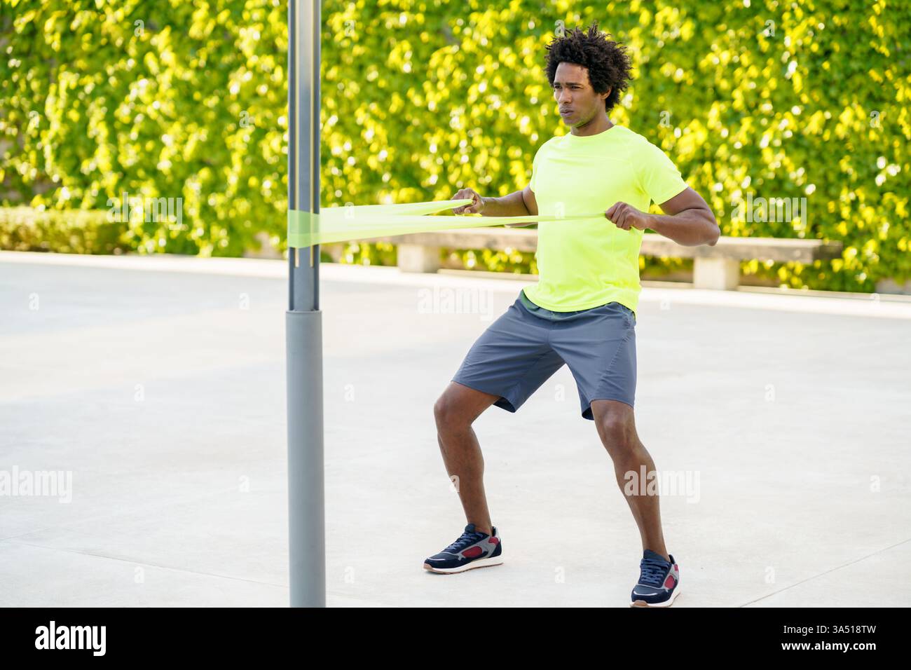 L'uomo nero si allena con una fascia elastica di resistenza all'aperto in un ambiente urbano. Ideale per allenamenti di fitness, campagne motivazionali e lifestyle all'aperto. Foto Stock
