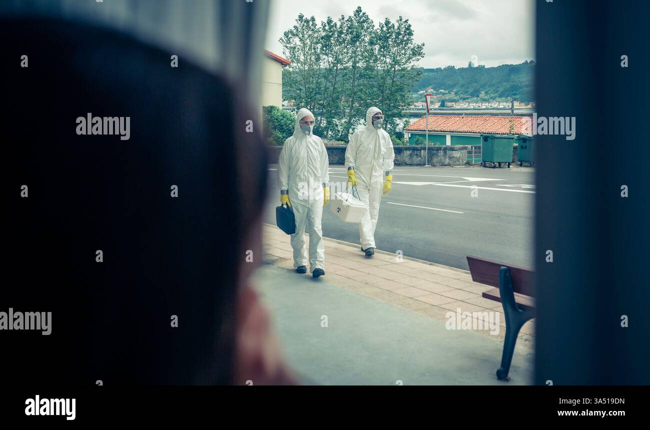 Gli operatori sanitari neri e caucasici in tute protettive camminano lungo una strada, pronti per il servizio. L'immagine cattura il personale medico in prima linea durante una crisi sanitaria, evidenziando l'equipaggiamento di protezione e il lavoro di squadra. Utile per l'assistenza sanitaria, la sensibilizzazione alle epidemie e i materiali di prevenzione delle infezioni. Foto Stock