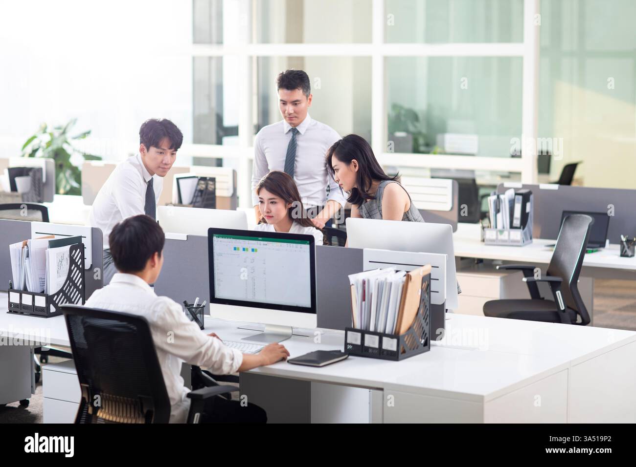 Gli uomini d'affari cinesi collaborano intorno a un computer in un ufficio luminoso. Ideale per storie sul lavoro di squadra, la partnership e la collaborazione basata sulla tecnologia. Foto Stock