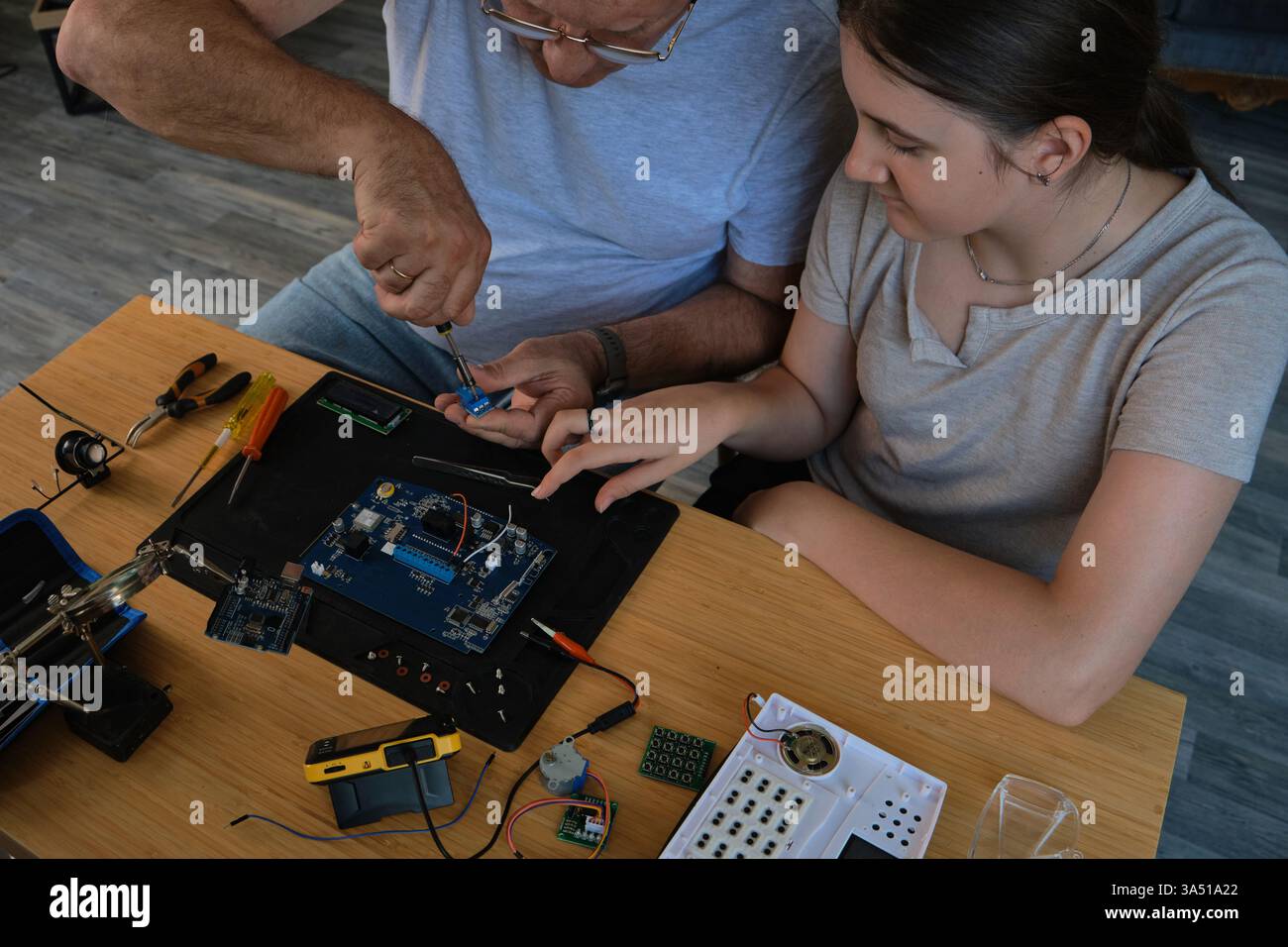 Nonno e nipote lavorano insieme a un progetto di elettronica a un tavolo. Ideale per famiglie, istruzione e fai da te Foto Stock