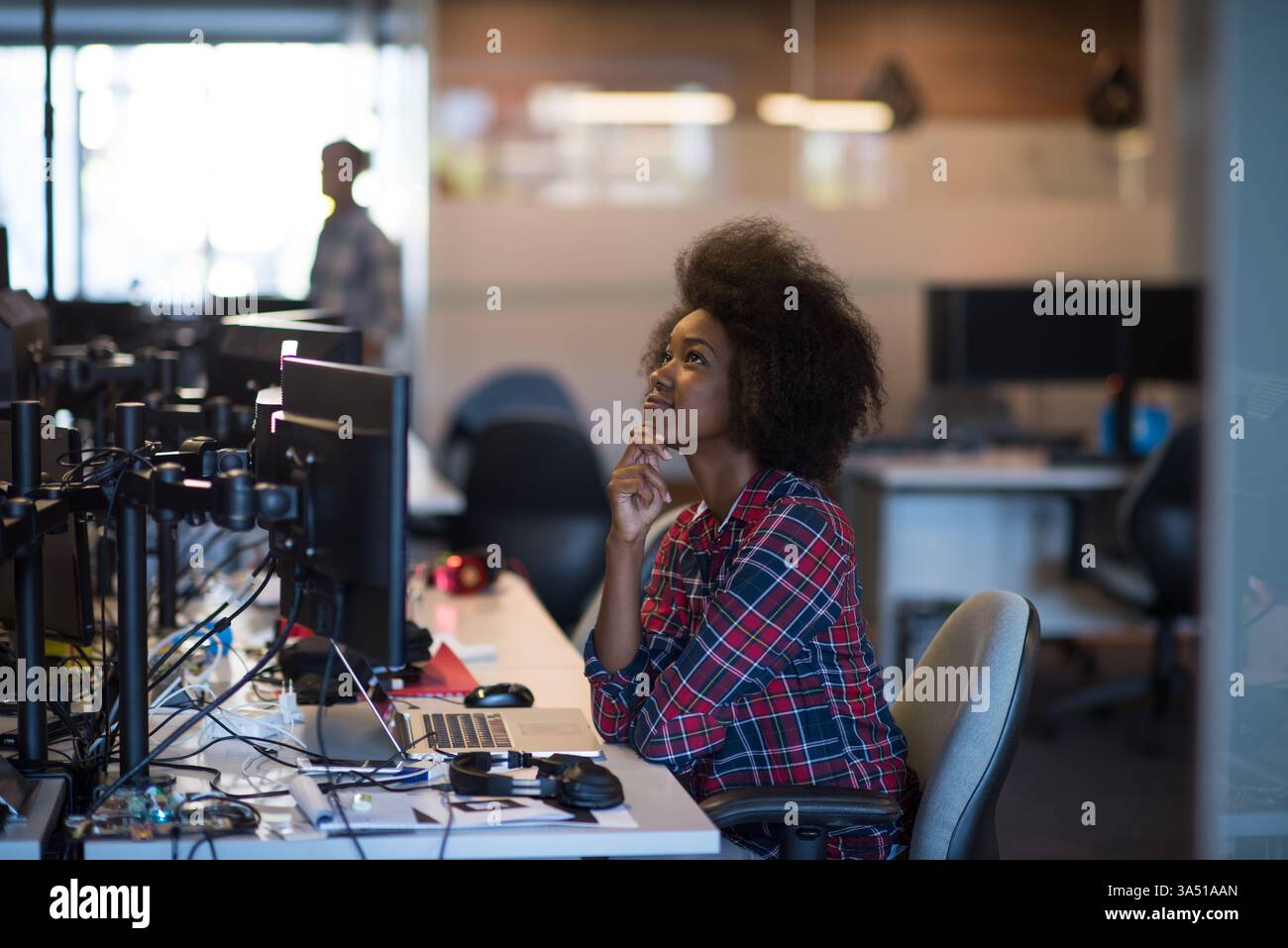 Ritratto di una donna afroamericana sicura di sé in un moderno ufficio aperto. Una scena professionale e allegra caratterizzata da uno spazio di lavoro elegante con un laptop e uno smartphone, che trasmette successo e concentrazione. Ideale per lo stile di vita aziendale, l'equilibrio tra vita lavorativa e imprenditoria femminile. Foto Stock