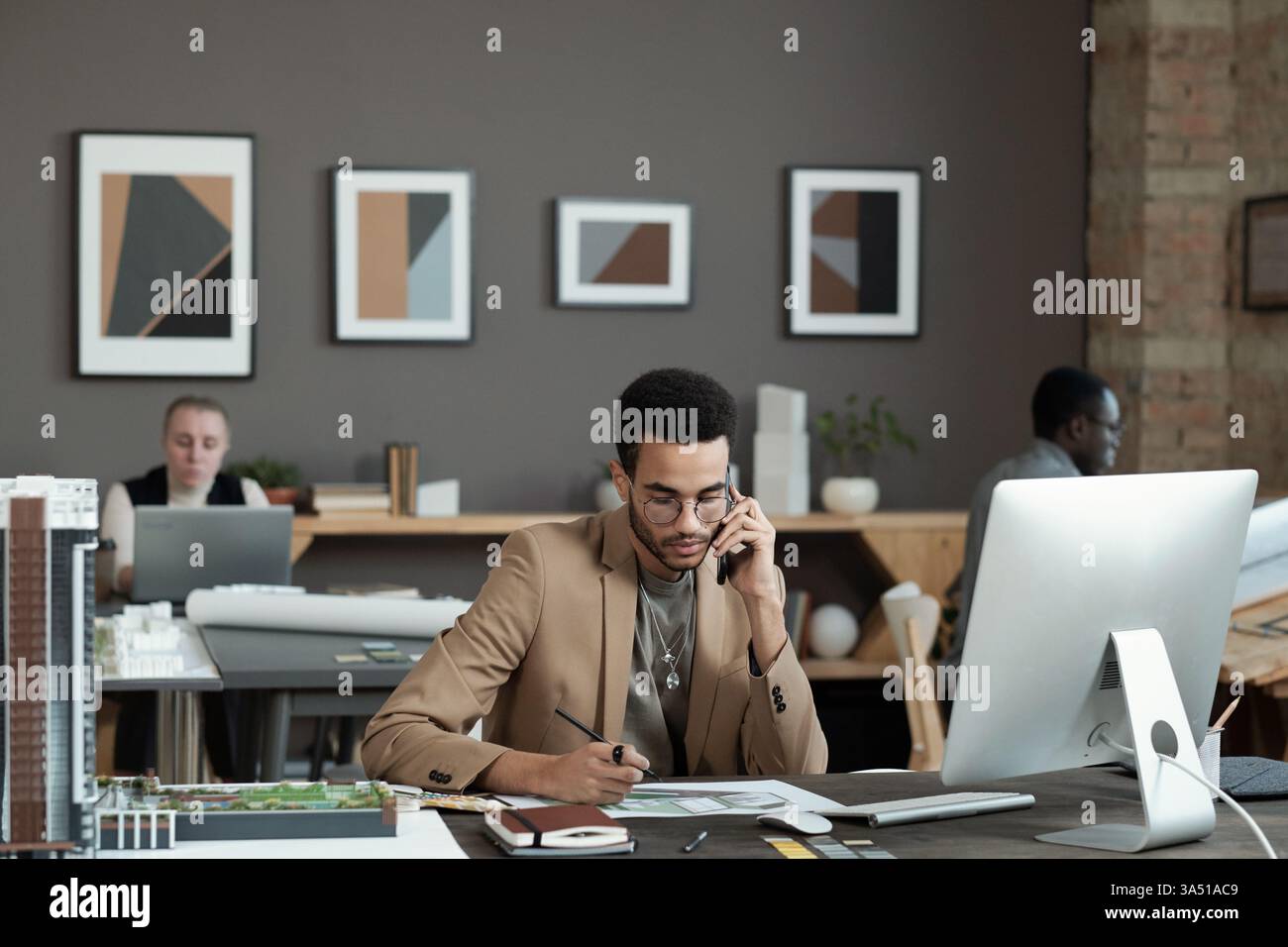 Un serio uomo di corsa mista parla al telefono in un ufficio contemporaneo. Progetta professionalità e concentrazione durante una chiamata al cliente. Foto Stock