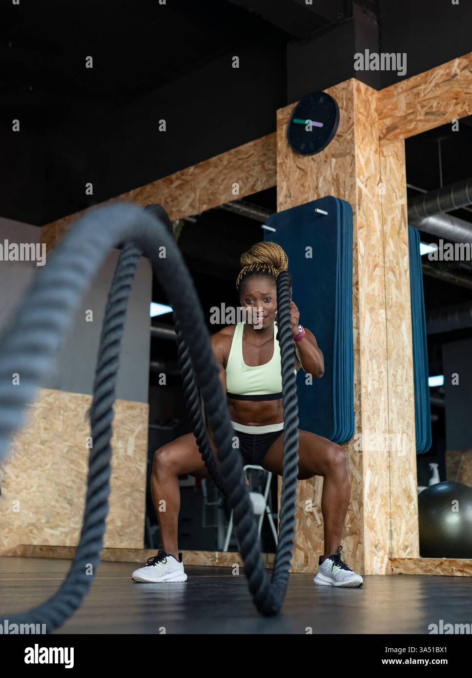 Donna nera che esegue esercizi di corda da battaglia in palestra durante un allenamento ad alta intensità. Immagine di fitness dinamica ideale per campagne HIIT, Strength e motivation. Cattura l'energia e lo sforzo atletico in palestra. Foto Stock