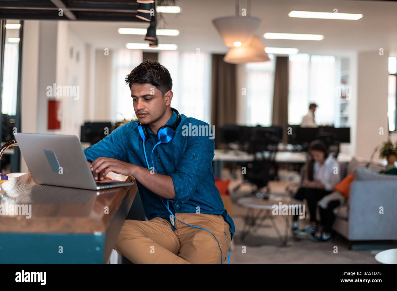 Uomo del Medio Oriente con le cuffie sul collo che lavora su un computer portatile seduto al tavolo del bancone in ufficio Foto Stock